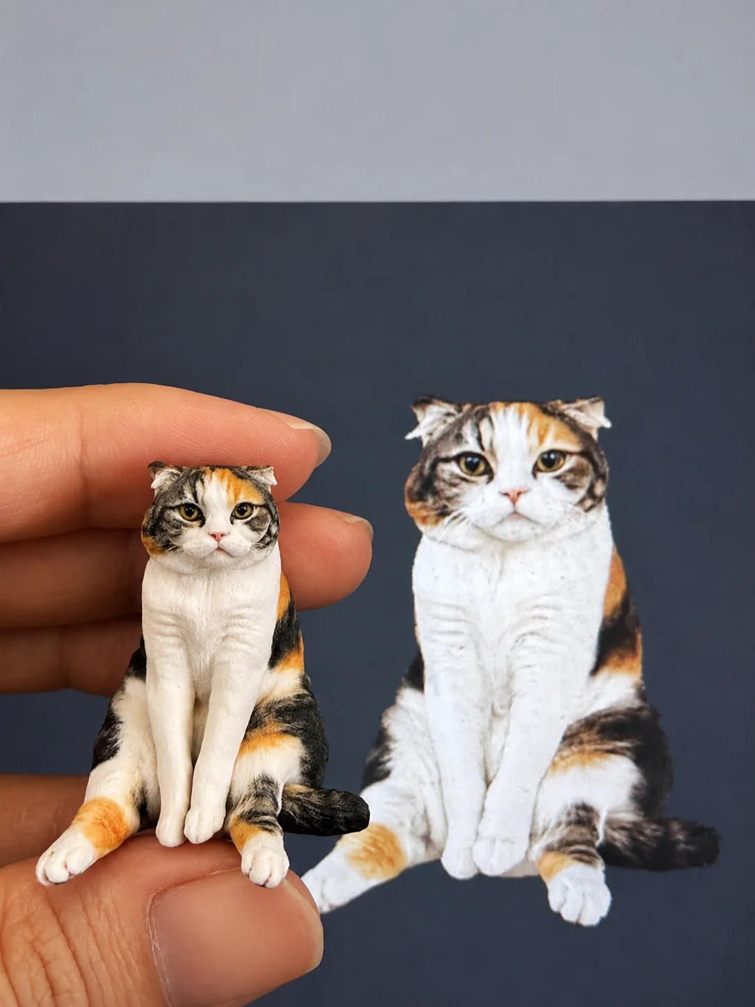 Calico cat figurine held beside its reference photo