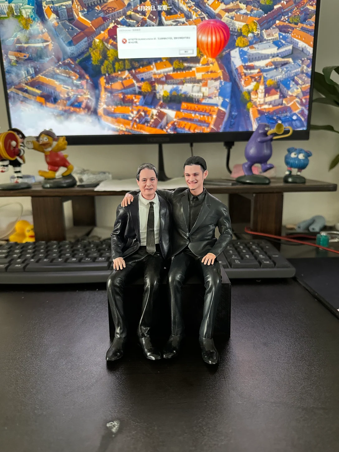 Two seated portrait figurines in suits with one arm around the other
